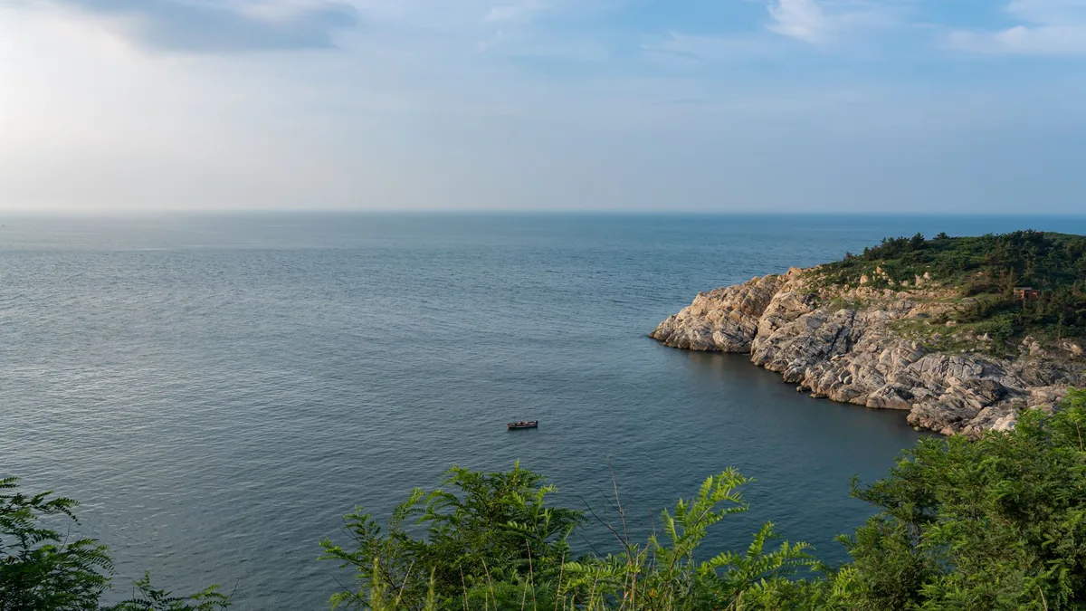 Tranquil view of a rocky cliff with lush greenery overlooking a calm ocean.